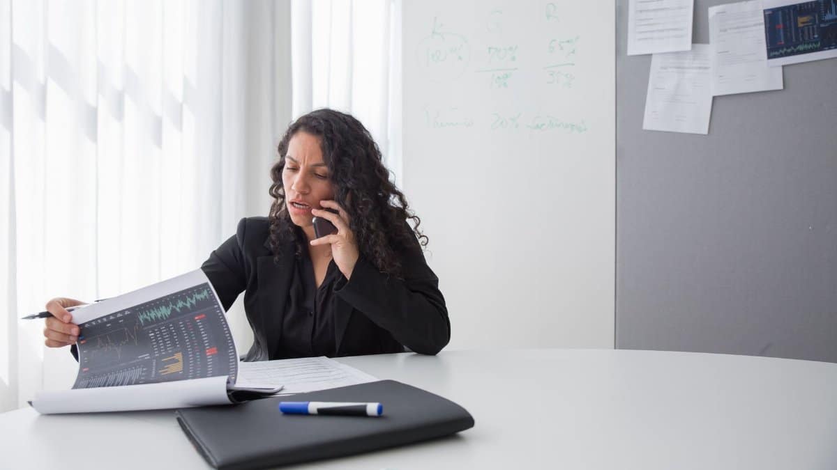 Focused businesswoman reviewing data charts during a phone call in a modern office setting.