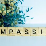 Scrabble tiles spelling 'compassion' with vibrant floral background.