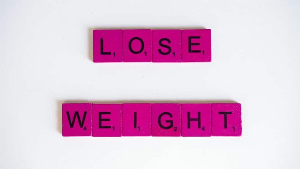 Creative image of the phrase 'Lose Weight' spelled with Scrabble tiles on a white background.