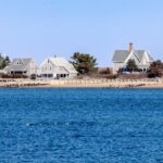 Picturesque Cape Cod lighthouse with traditional homes by the shoreline under a clear sky.