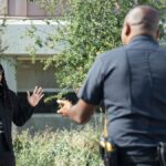 A police officer engages with a civilian raising hands outdoors, signifying communication or questioning.