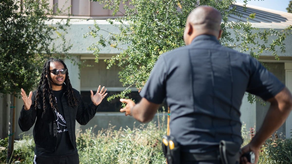A police officer engages with a civilian raising hands outdoors, signifying communication or questioning.