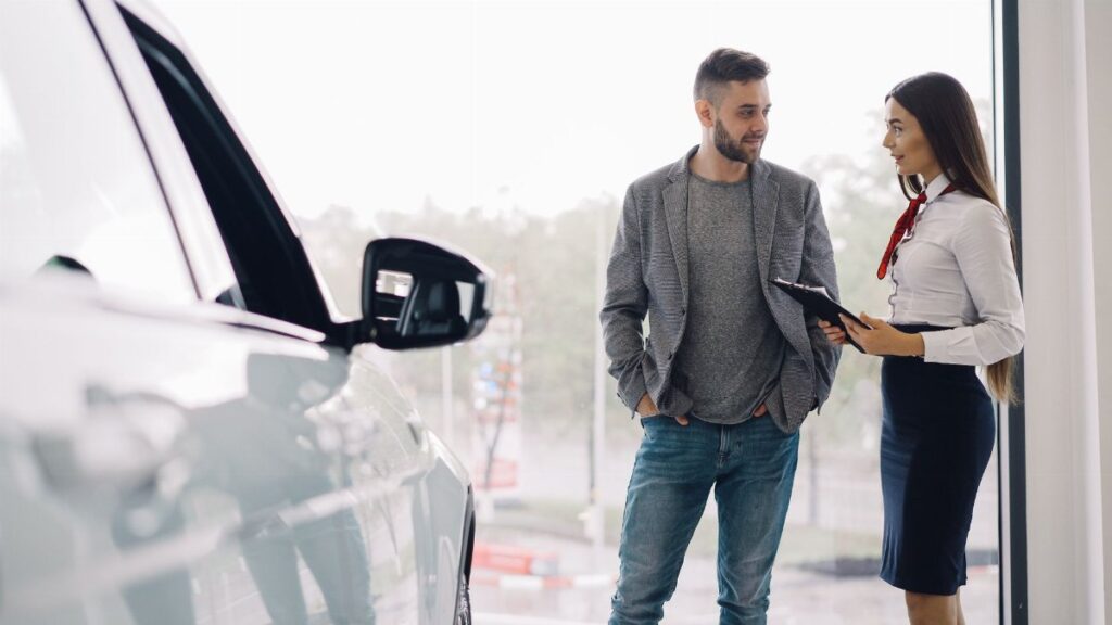 Man consulting with car salesperson in a showroom, discussing car options.