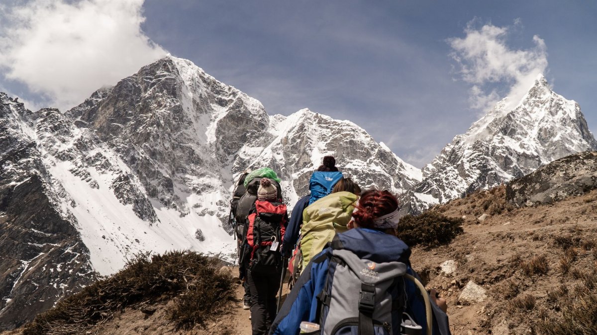 Group of hikers trekking on a sunny day with snow-capped mountains in the background. Outdoor adventure scene.