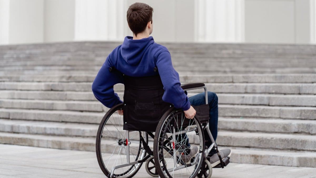 Back view of a young man in a wheelchair facing steps in a city setting.