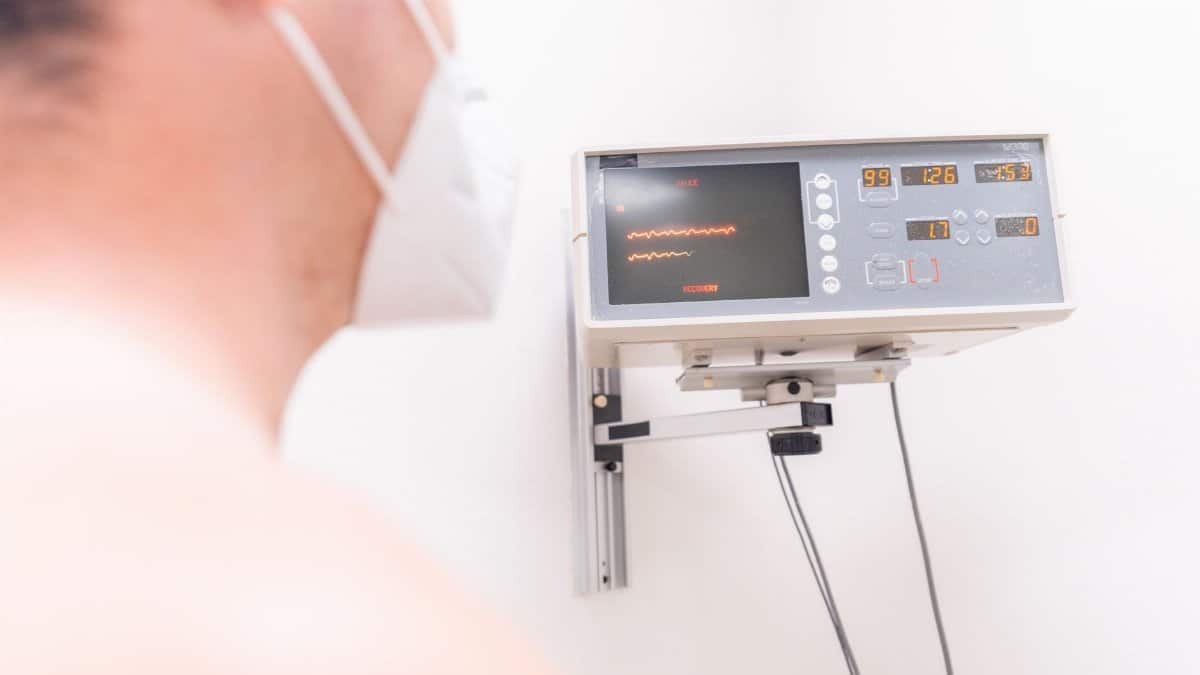 A masked patient in a clinic being monitored by an electronic device.