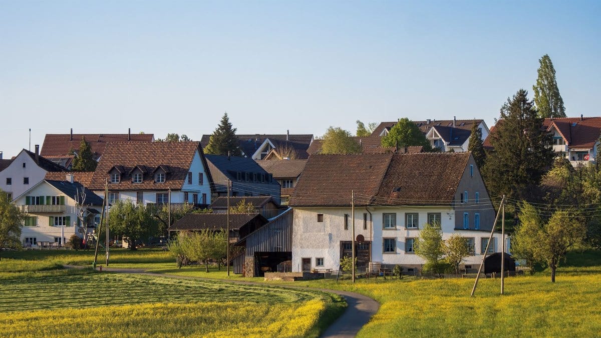 Picturesque rural village with traditional houses and green fields under clear blue sky.