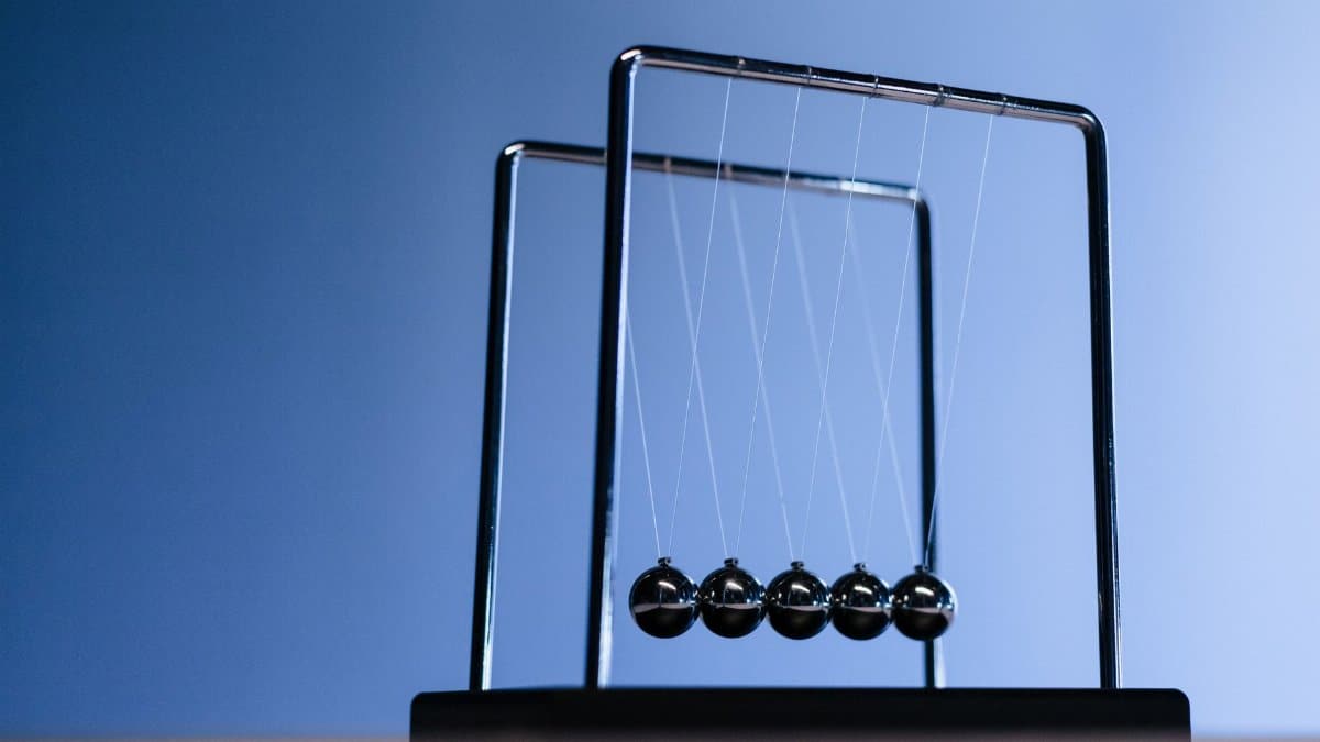 Silhouette of Newton's cradle with metallic balls against a blue background, showcasing physics in action.