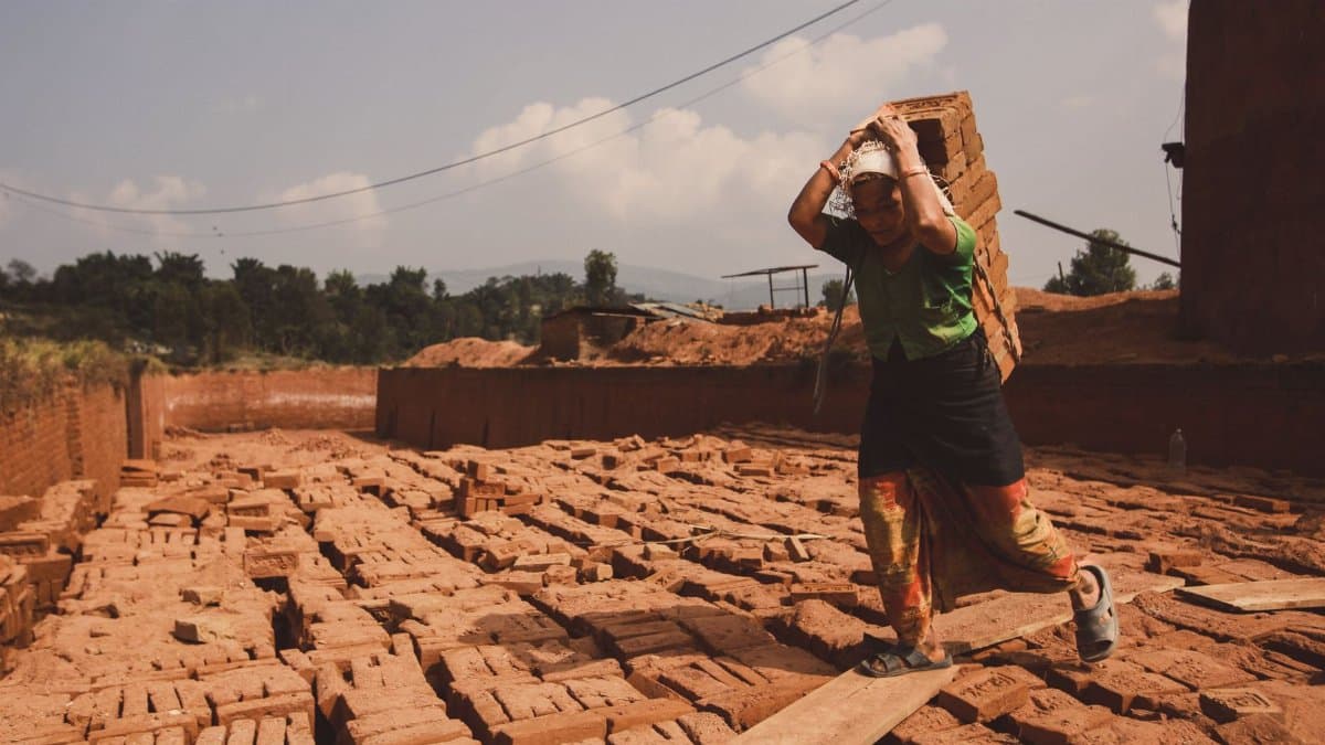 A woman laborer carrying heavy bricks in an outdoor kiln, showcasing hard work.