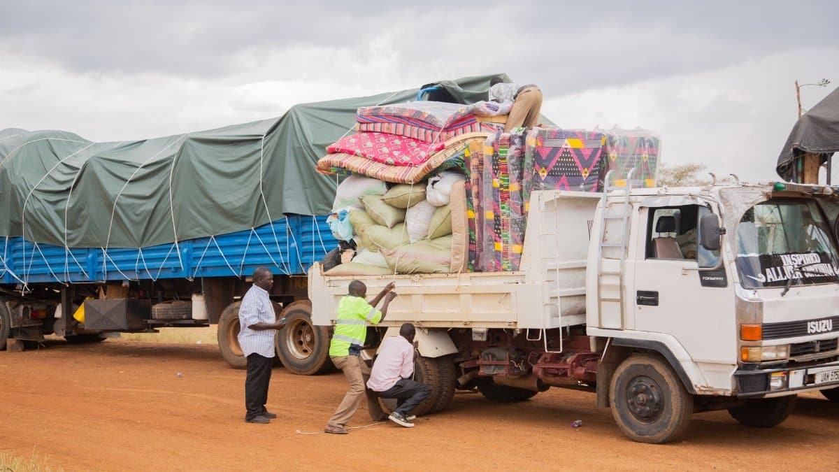 People loading supplies onto a truck in a rural area under cloudy skies.