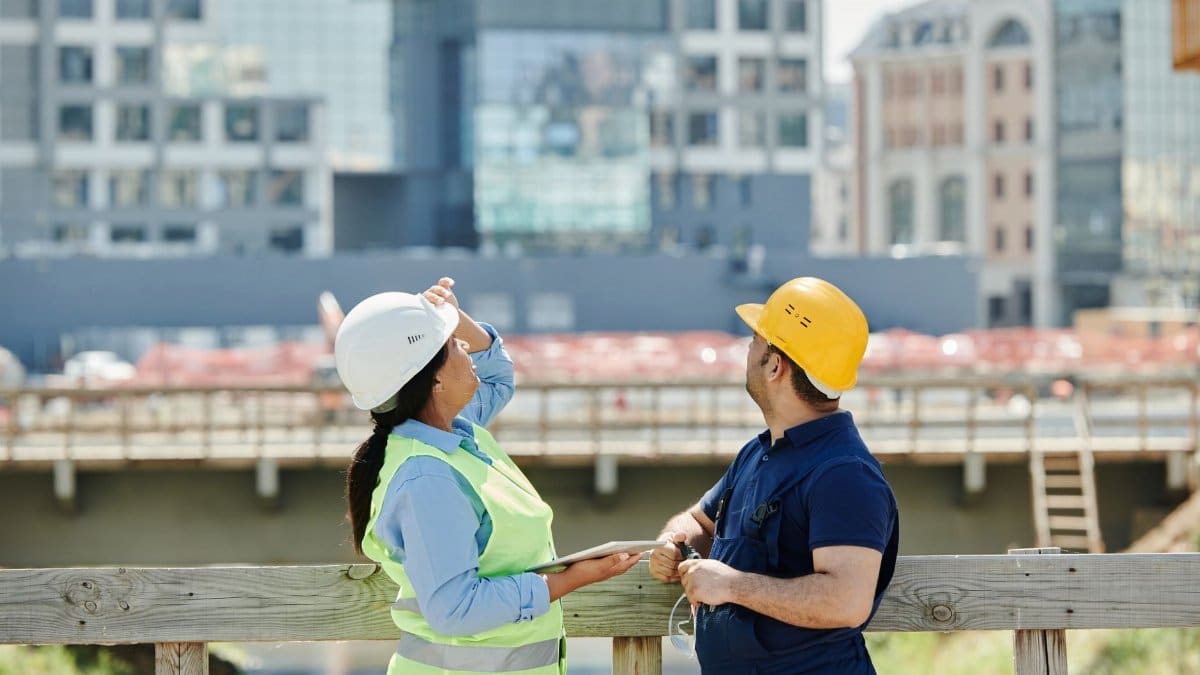 Engineers at a construction site reviewing architectural plans with modern cityscape background.
