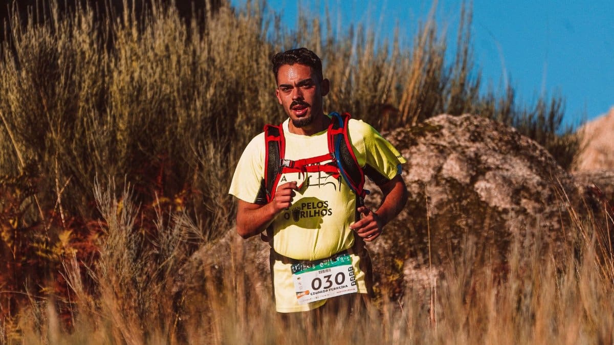 A man participates in a trail marathon, running through rugged terrain in bright sunlight.