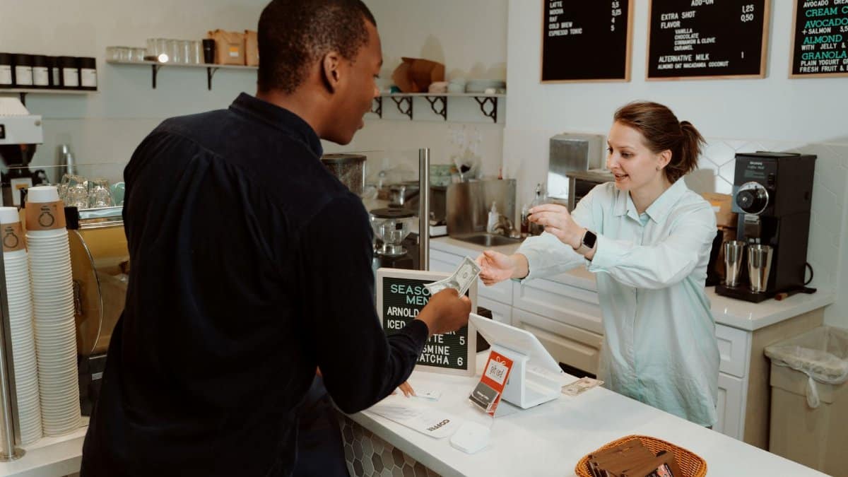 A customer pays for coffee at a café counter, transaction with barista.