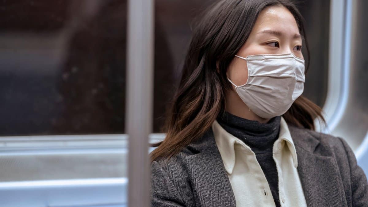 Young Asian woman in protective mask commuting on public transit, exemplifying the new normal.