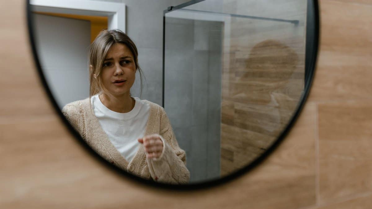 A woman gazes into a mirror, reflecting emotions and self-awareness in a bathroom setting.