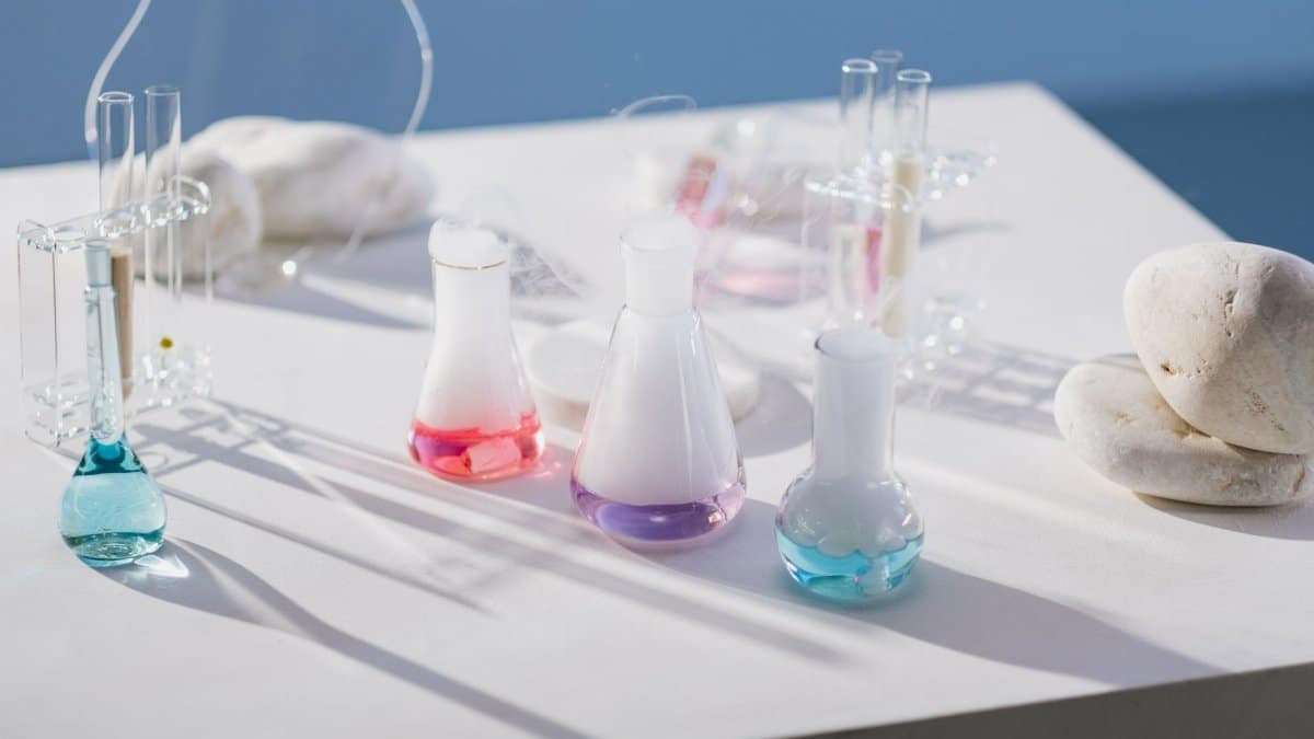 Vibrant chemical liquids in flasks and test tubes on a sunny white table with stones.