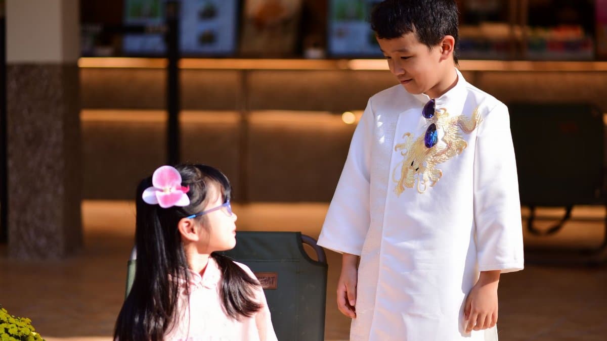 Two children in traditional Asian clothing indoors, engaging in a conversation.