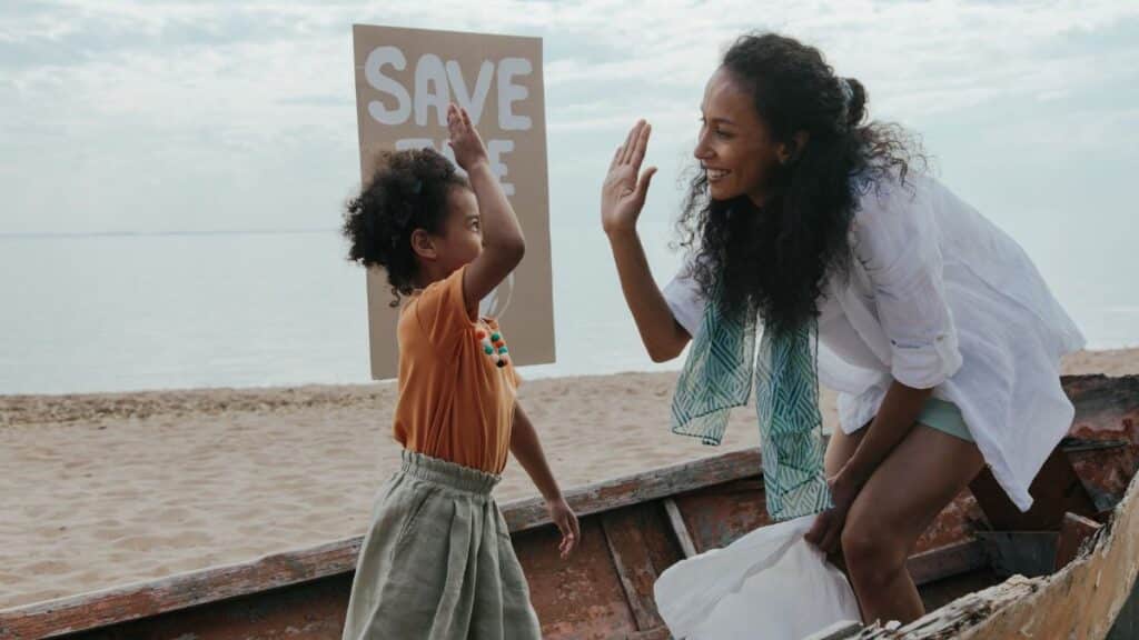 Mother and child high-five during a fun beach cleanup with a save the planet sign.