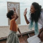 Mother and child high-five during a fun beach cleanup with a save the planet sign.
