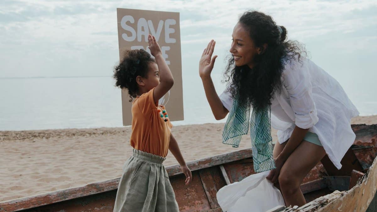 Mother and child high-five during a fun beach cleanup with a save the planet sign.