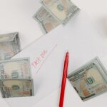 A top-down view of scattered US dollar bills with a 'past due' envelope, red pen, and notepad.