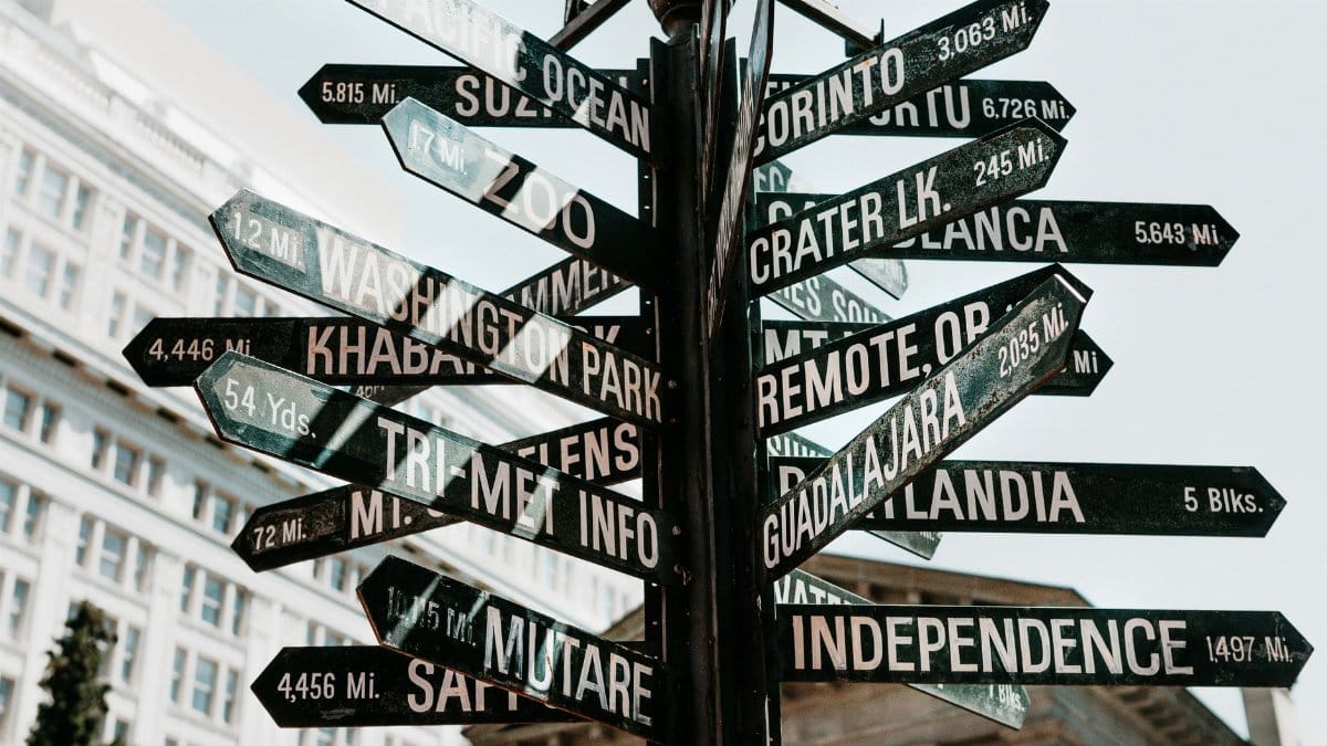Close-up of a directional signpost with city names and distances in an urban setting.