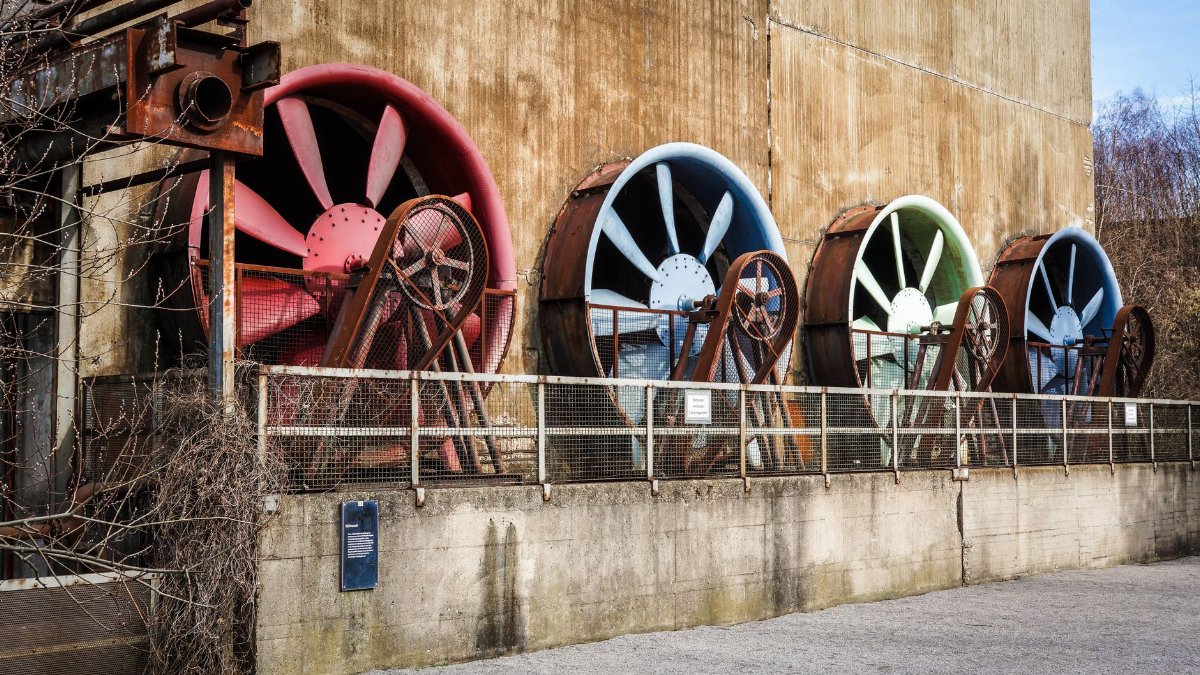 A row of large colorful ventilation fans on a rustic industrial building exterior.