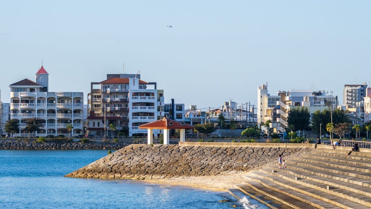 Charming coastal cityscape with waterfront steps, modern buildings, and blue sea under a clear sky.