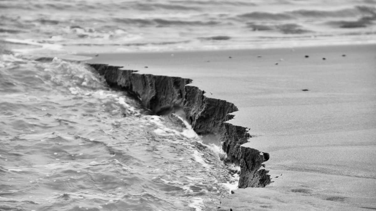 Dramatic black and white photo of coastal erosion along the seashore with waves.