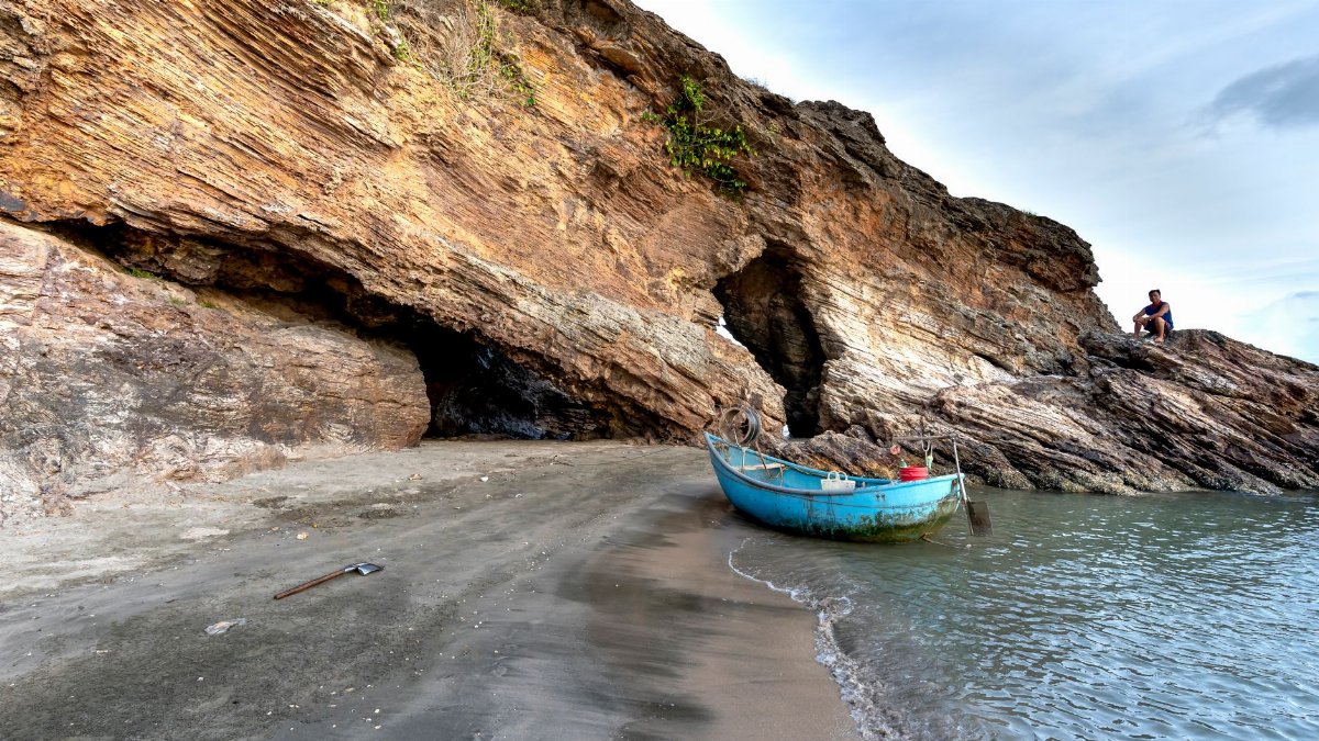A serene coastal scene featuring a blue boat near rock caves on a sandy beach.