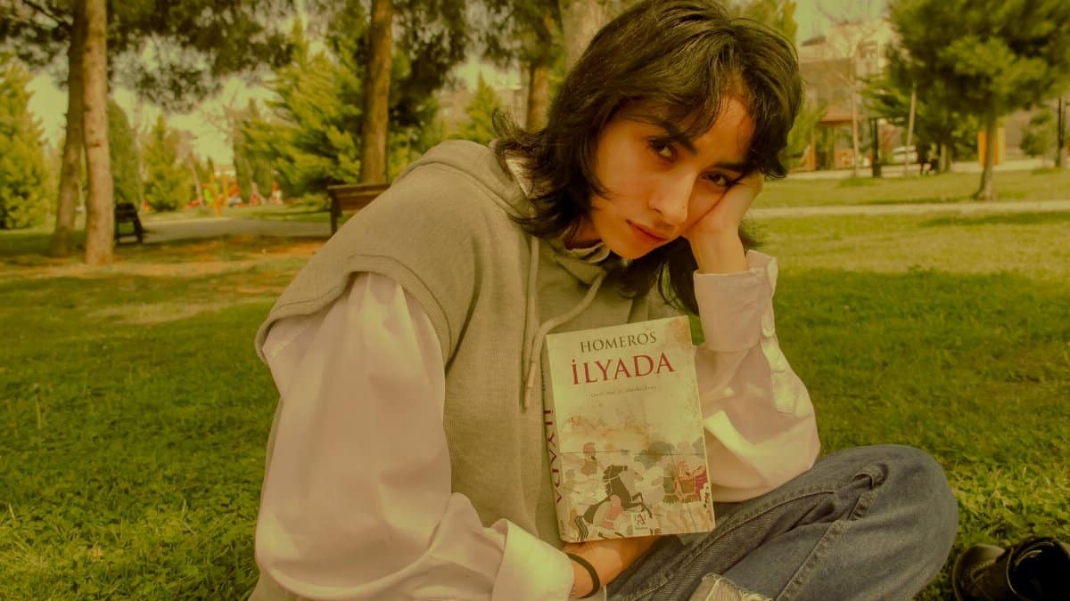 Young woman in a park reading 'Iliad' by Homer, enjoying a peaceful outdoor setting.