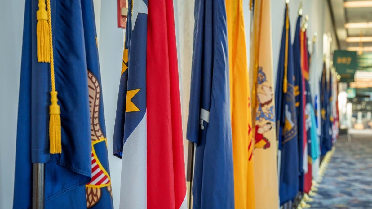 Colorful display of multiple state flags lining a corridor in daylight.