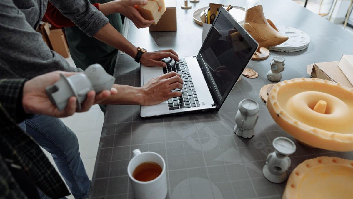 Hands on laptop in a creative workspace with 3D models and prototypes.