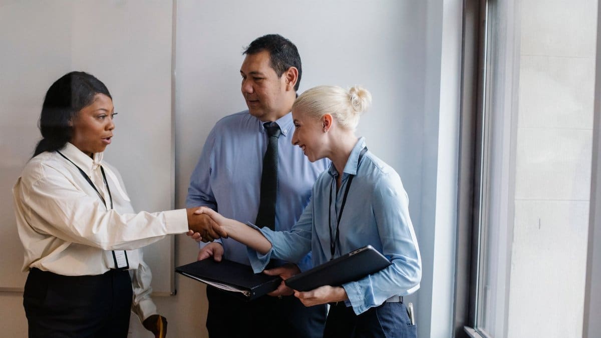 Happy young multiethnic female managers in classy outfits smiling and shaking hands during meeting with ethnic colleague in office