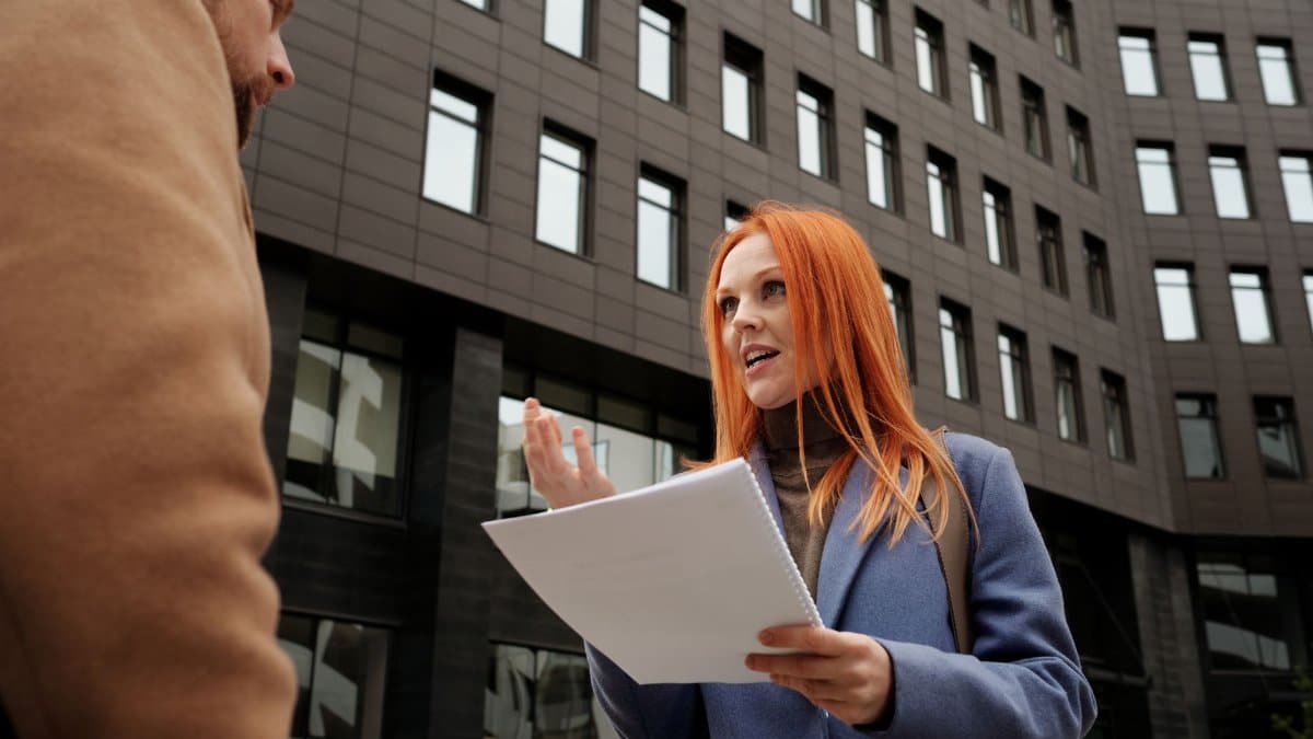 Professional woman and colleague in conversation holding documents outdoors