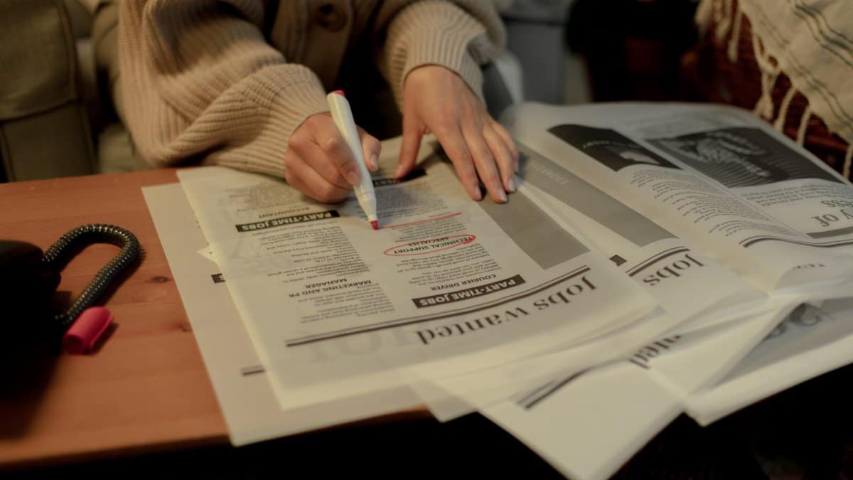 A person highlights job listings in newspaper, focusing on job search indoors.