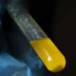 A gloved hand holds a test tube filled with yellow liquid, symbolizing scientific research.