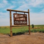 Wooden welcome sign in a Colorado field under a bright, clear sky.