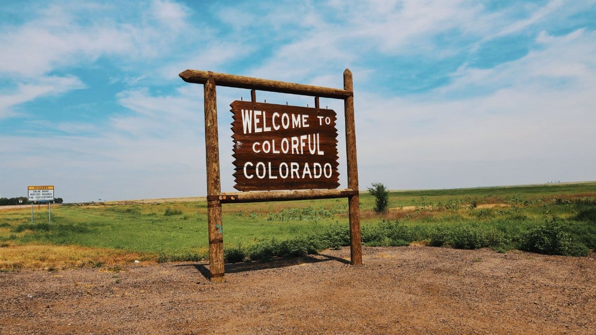Wooden welcome sign in a Colorado field under a bright, clear sky.