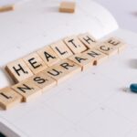 Scrabble tiles spelling 'Health Insurance' on a calendar with pills.