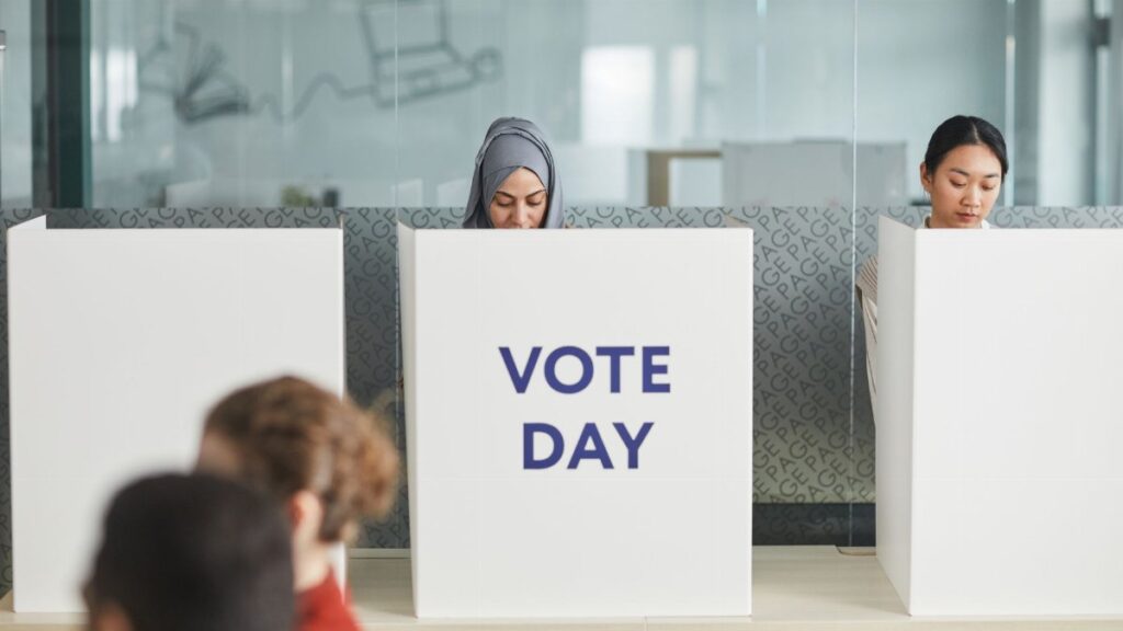 Two women casting their votes in an office during election day, focusing on diversity and civic engagement.