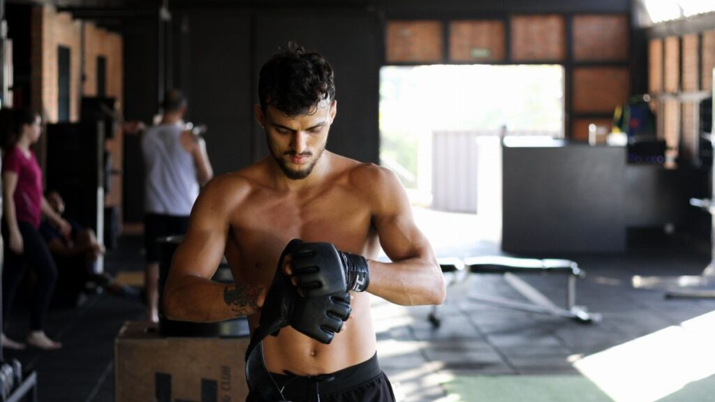 Shirtless man preparing for an intense workout session in a gym, wearing boxing gloves.