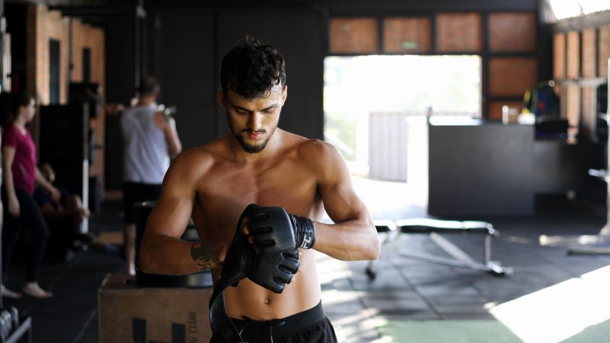 Shirtless man preparing for an intense workout session in a gym, wearing boxing gloves.