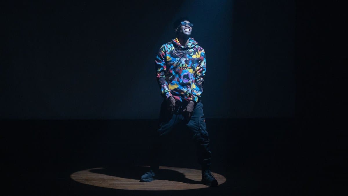 Energetic hip hop musician in colorful attire illuminating the stage under a dramatic spotlight.