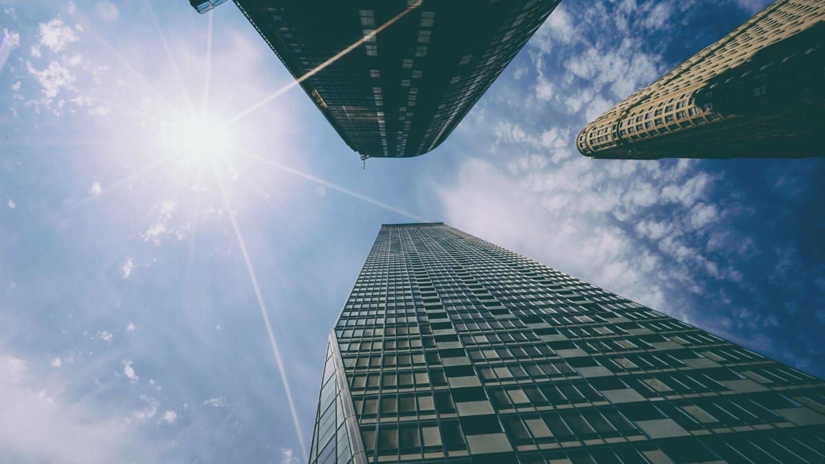 Low angle view of tall skyscrapers with sun glare against a bright blue sky.