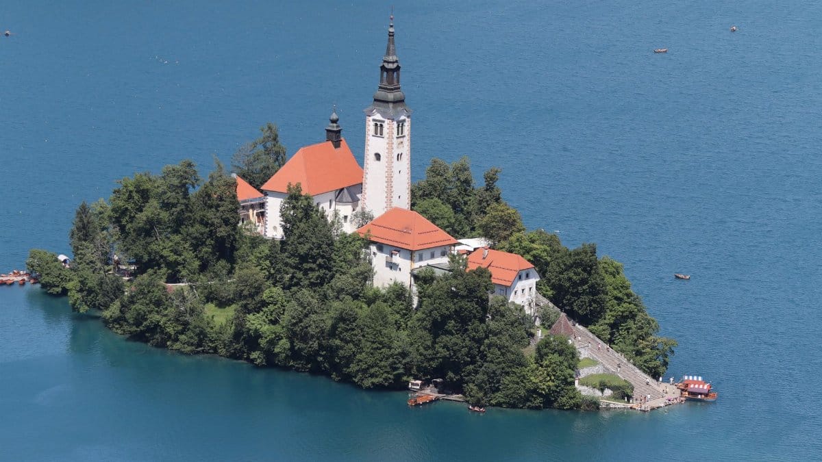 Stunning aerial view of Bled Island and church on Lake Bled, Slovenia, surrounded by crystal blue water and lush greenery.