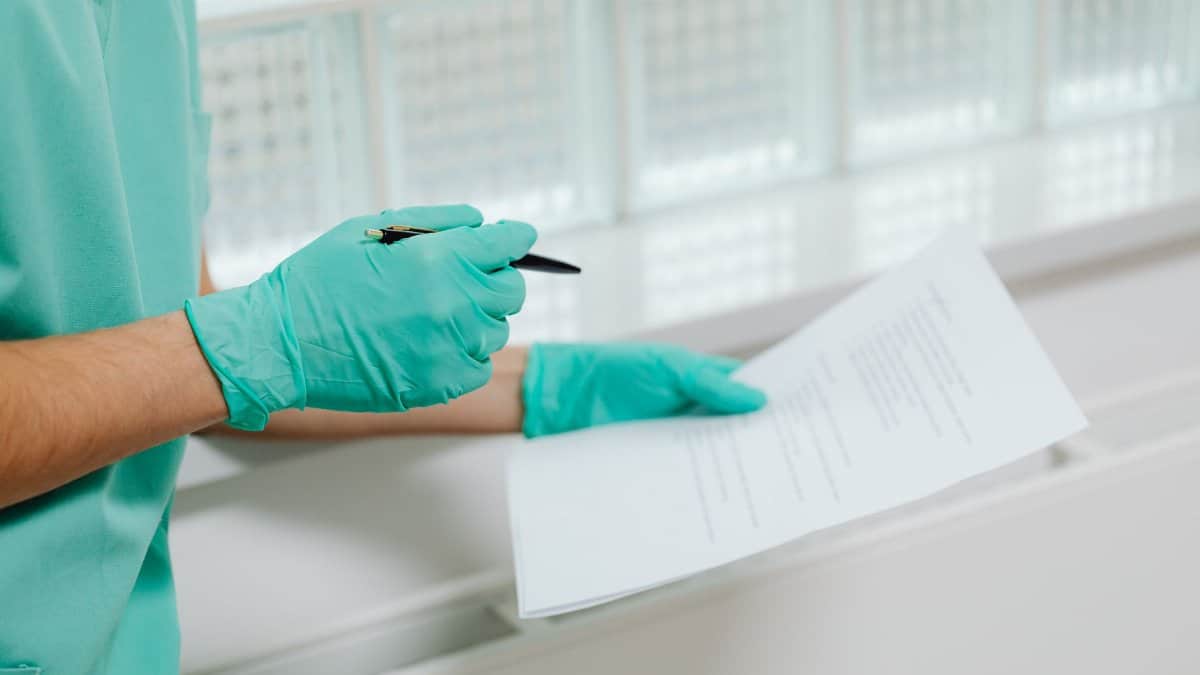 Close-up of a healthcare professional in gloves holding and reading a medical document indoors.