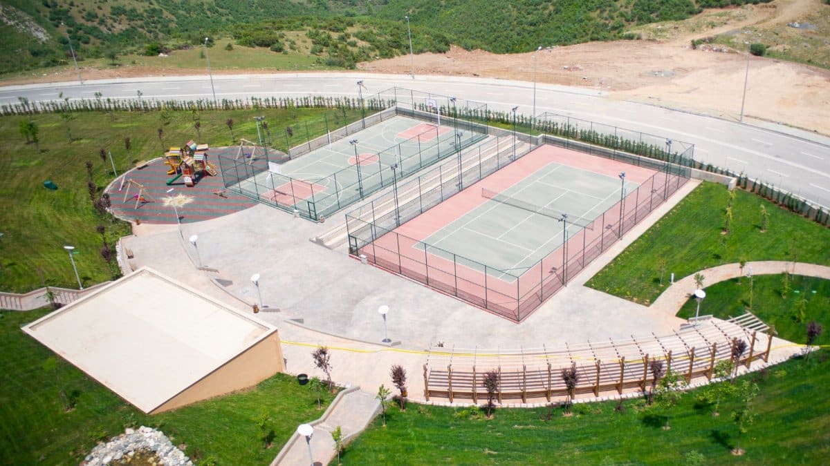 High-angle shot of tennis courts and playground in a park setting.