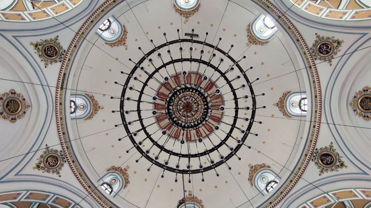 Intricate view of an ornate dome ceiling with a central chandelier in a building interior.