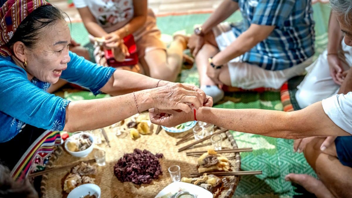A group of adults share a traditional meal on a woven mat indoors.